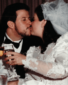 a bride and groom kiss while holding a glass of wine