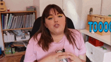 a woman in a pink shirt is sitting in a chair in front of a bookshelf with the word toooo on it .