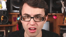a man wearing glasses makes a funny face in front of a speaker