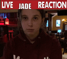 a girl wearing a red hoodie stands in front of a live jade reaction sign