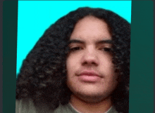 a man with long curly hair and a green shirt looks at the camera