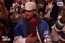 a man wearing a hat with the letter s on it sits in the audience at the iheartradio music awards