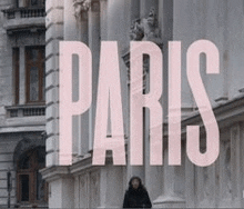 a woman is standing in front of a building with the words `` paris '' written on it .