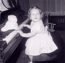 a little girl is playing a piano with a teddy bear in the background