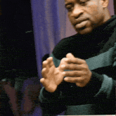 a man wearing a black and green striped sweater holds his hands together