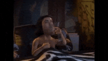 a naked man is sitting on a bed holding a glass of wine .