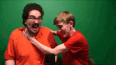 a man in an orange shirt is laughing while another man in a red shirt holds his neck