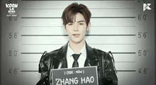 a man in a black jacket and tie holds a sign that says zhang hao
