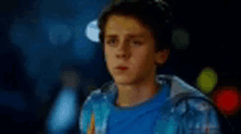 a young boy wearing a blue shirt and a blue jacket is standing in a dark room .