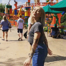 a woman with tattoos on her arms is standing in front of a roller coaster at an amusement park .