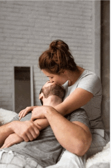 a woman is kissing a man on the neck while laying on a bed