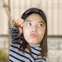 a young girl wearing a striped shirt is giving a thumbs down sign