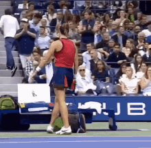 a woman in a red tank top and blue skirt is standing on a tennis court in front of a crowd .