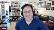 a man wearing headphones is smiling in a living room with a sign that says corey on it