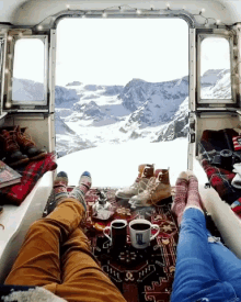 a person laying on a rug with two cups of coffee in front of a view of snow covered mountains