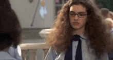 a girl with long curly hair and glasses is standing next to another girl in a classroom .