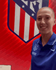 a woman stands in front of a red white and blue shield that says ' atlético madrid ' on it