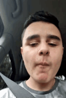 a young man wearing a seat belt is making a funny face while sitting in a car .