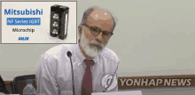 a man sitting at a table with a microphone in front of a sign that says mitsubishi