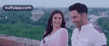 a man and a woman are standing next to each other on top of a hill and smiling .