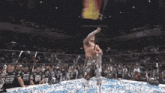 a shirtless wrestler is holding a rope in a wrestling ring in front of a crowd .