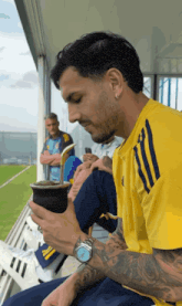 a man wearing a yellow adidas shirt is drinking from a cup