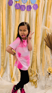 a little girl making a peace sign in front of a nancy banner