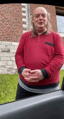 a man with long hair is standing in front of a brick building in a red sweater .