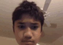 a young boy is making a funny face in front of a ceiling fan in a room .