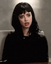 a woman with black hair and bangs is sitting at a table with her mouth open .
