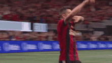 a man in a red and black jersey is standing on a soccer field with his arms in the air