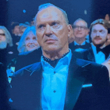 a man in a tuxedo and tie is sitting in a crowd of people