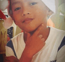 a young boy wearing a santa hat is looking at the camera with his hand on his chin .