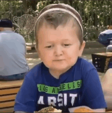 a little boy wearing a blue shirt that says los angeles arsit is eating a hamburger .