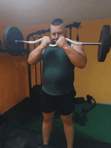 a man in a green tank top is holding a barbell over his head