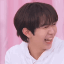 a close up of a young man laughing while wearing a white shirt .