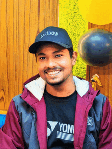 a man wearing a black yonex shirt and a hat smiles