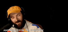 a man with a beard is wearing headphones and a yellow hat while talking into a microphone
