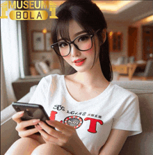 a woman wearing glasses is holding a cell phone in front of a museum bola logo