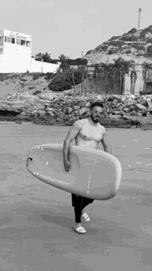 a man without a shirt is carrying a surfboard on the beach