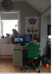 a young boy is sitting at a desk with a computer and a poster that says meet stuart kevin and bob .