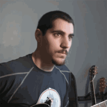 a man with a beard is holding a guitar and wearing a blue shirt with a circle on it