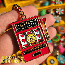 a person is holding a slot machine keychain with hearts and a dollar sign