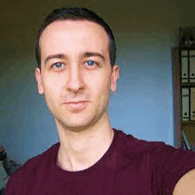 a man in a maroon shirt is taking a selfie in front of a wall .