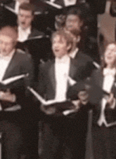 a group of people in tuxedos are singing in a choir