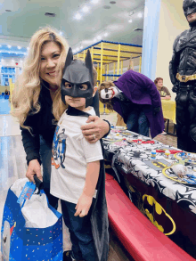 a woman holds a child in a batman mask