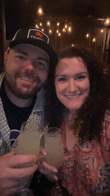 a man wearing a hat that says ytl on it toasts with a woman