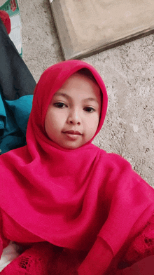 a little girl wearing a pink hijab is sitting on the floor