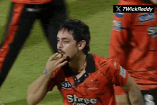 a man wearing a red shree com jersey eating something
