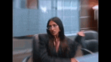 a woman is sitting at a desk wearing glasses and a black suit .